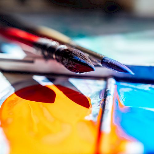 Paintbrushes and bright colors on a palette, ready for a watercolor session; vibrant oranges, blues, and reds ignite the canvas.