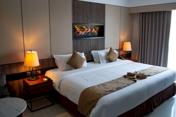 A cozy hotel room with a large bed, warm lighting, decorative pillows, and a modern wall art piece above the headboard.