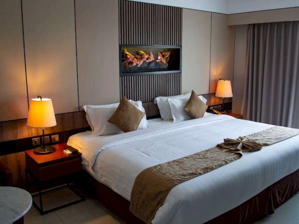 A cozy hotel room with a large bed, warm lighting, decorative pillows, and a modern wall art piece above the headboard.