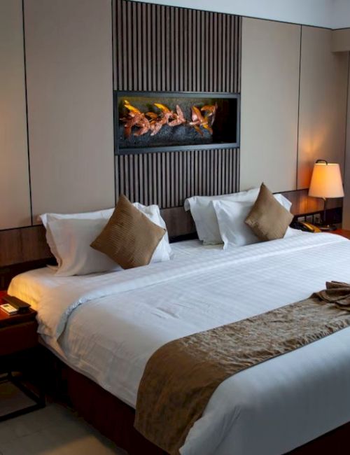 A neatly arranged hotel room features a large bed, two side tables with lamps, a decorative wall piece, and a curtain covering the window.