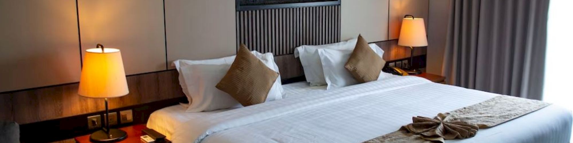 A neatly made bedroom with a large bed, two bedside lamps, decorative pillows, and a wall-mounted feature above the headboard.