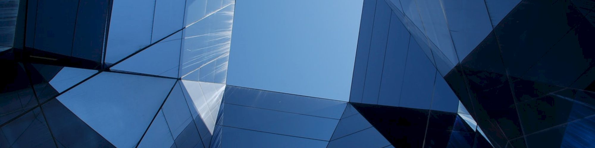 The image shows a view of modern architecture with reflective glass facades converging towards an open sky, creating a geometric pattern.
