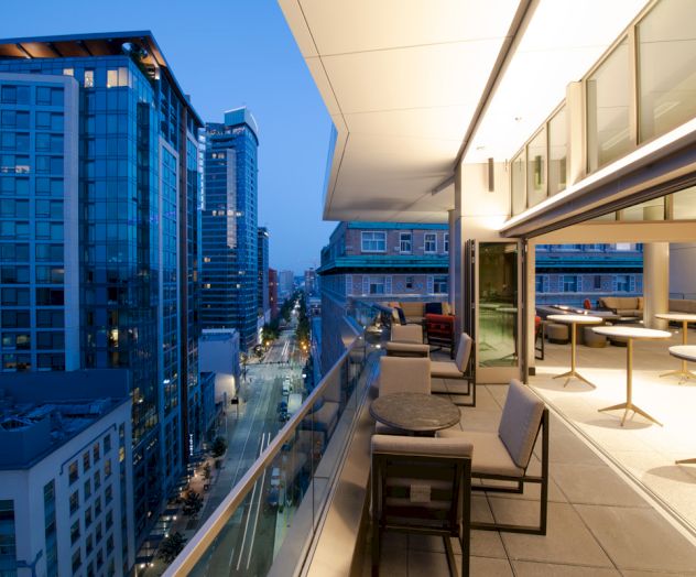A modern rooftop terrace with seating overlooks a cityscape of tall buildings during twilight.