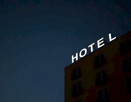 The image shows the side of a building at night with a sign that says "HOTEL" in white letters, against a dark sky.