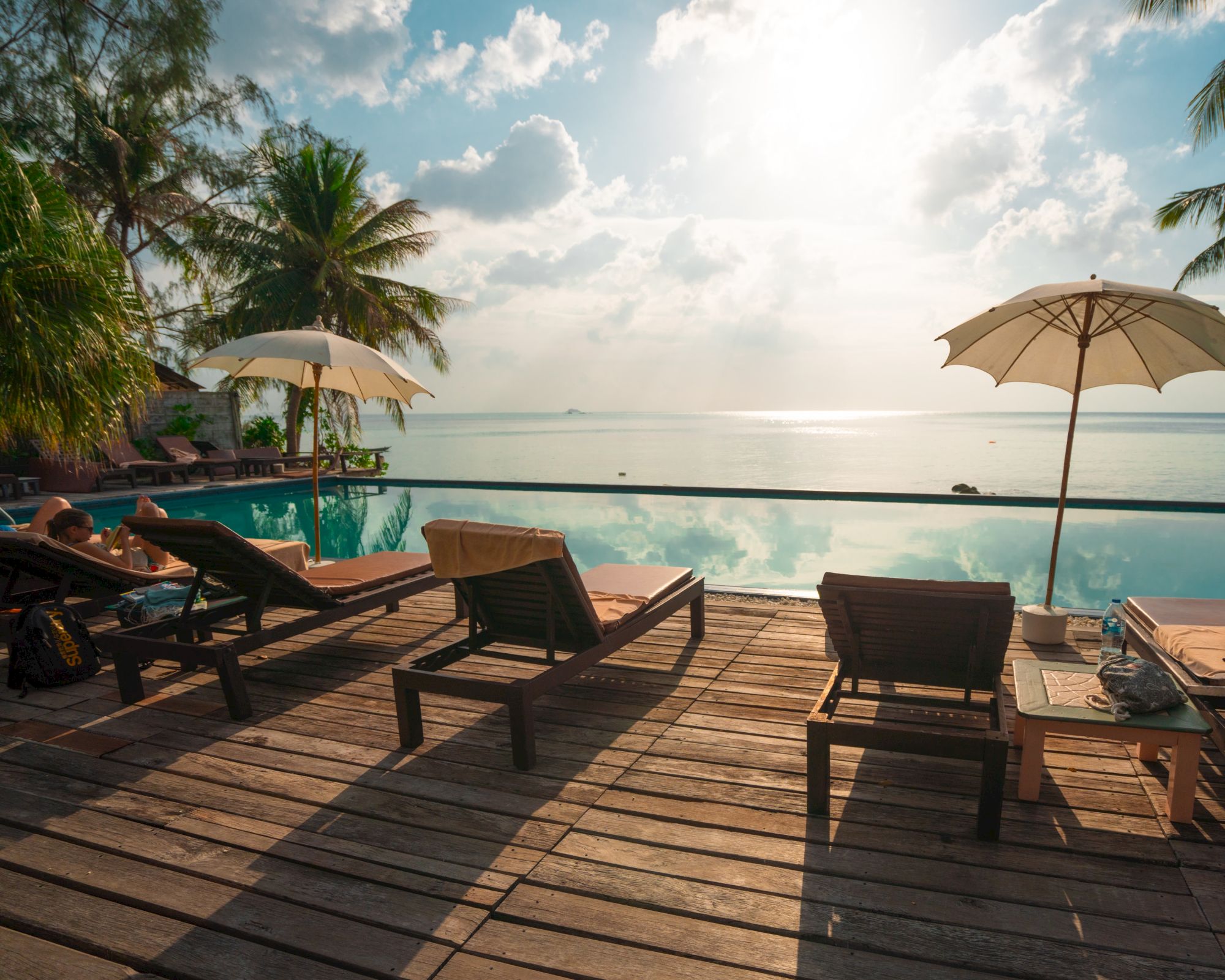 A serene beachfront scene with lounge chairs, umbrellas, and a pool, overlooking the ocean with a stunning sky in the background.