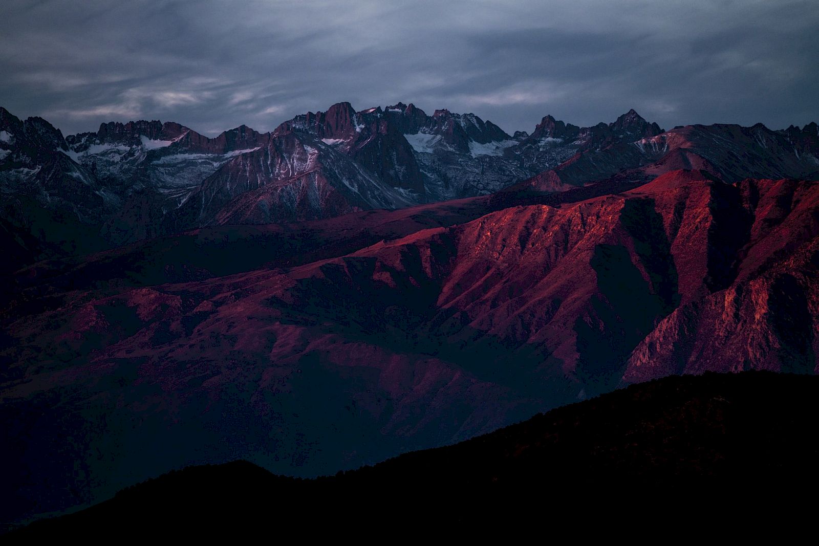 A mountain range at dusk with dramatic cloud cover and peaks illuminated in shades of red.