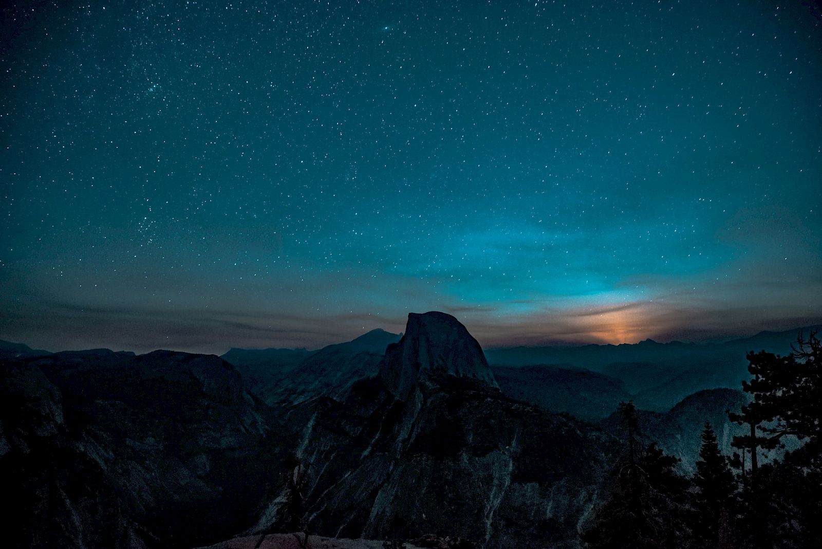 A starry night sky over a mountainous landscape with a glowing horizon creates a serene and captivating scene.