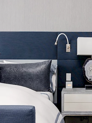 A stylish bedroom features a blue headboard, white bedding with blue pillows, a modern lamp, and a nightstand with a stone lamp design.