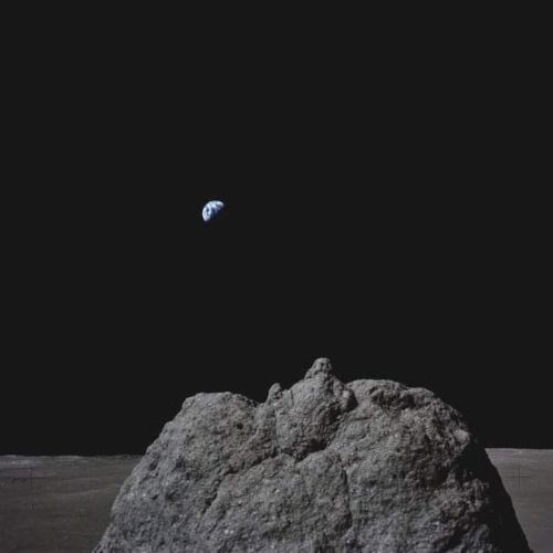 A rock on the lunar surface with the Earth visible in the black sky above, showcasing the vastness of space.