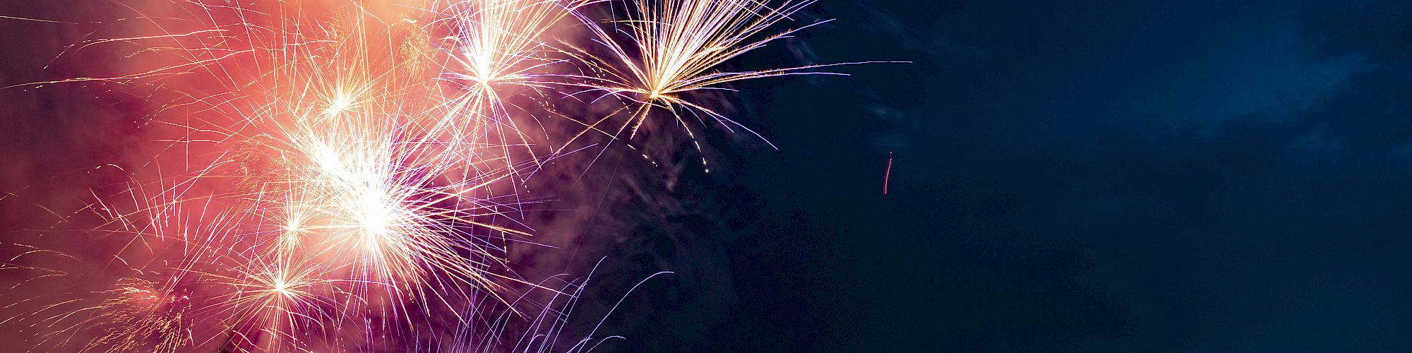 Fireworks illuminate the night sky over a large, well-lit building, creating a festive atmosphere against a dark backdrop.