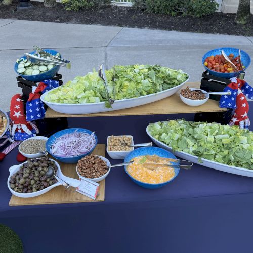 A salad bar with lettuce, cherry tomatoes, cucumbers, onions, croutons, olives, bacon, cheese, and nuts in various bowls ends the sentence.