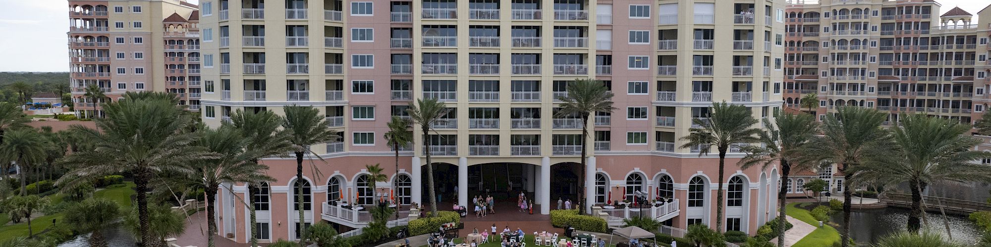 A large gathering is taking place on a lawn in front of a tall building, with tables and an American flag visible.