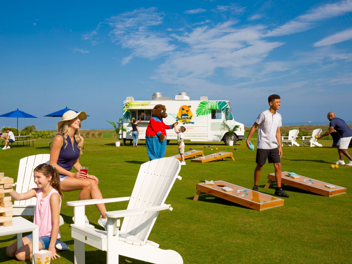 People enjoying outdoor games on a lawn with a food truck in the background under a blue sky.