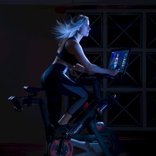 A person is riding an exercise bike indoors, watching a screen.