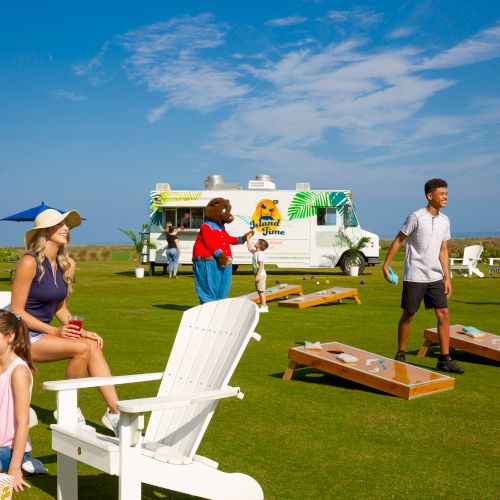 People are playing lawn games near a food truck on a sunny day, enjoying outdoor leisure activities with clear blue skies above.