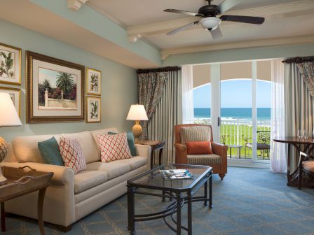 A cozy living room with a sofa, armchair, coffee table, lamps, and ocean view through large windows, featuring elegant decor.