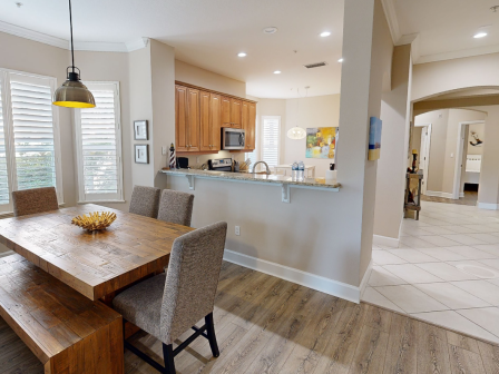 A dining area with a wooden table and chairs, a kitchen with wooden cabinets, and a hallway. Light and neutral tones dominate the space.
