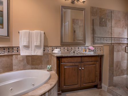 A bathroom with a bathtub, towels, a sink, cabinet, mirror, and a glass-walled shower. Neutral tones and decorative tiles enhance the decor.