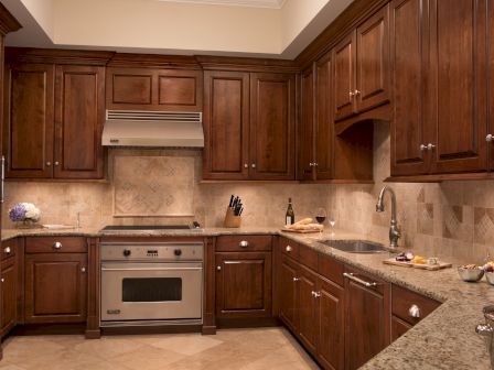 A kitchen with wooden cabinets, a stove, a sink, and countertops adorned with various items and a wine glass near the sink.