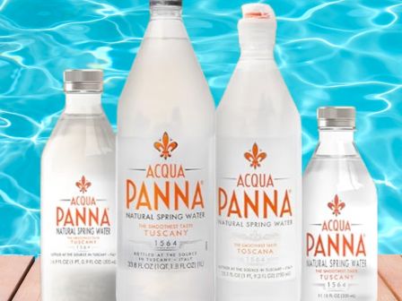 Four bottles of Acqua Panna natural spring water are placed on a wooden surface with a pool in the background.
