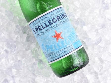 A green glass bottle of S.Pellegrino sparkling water rests on a bed of ice cubes.