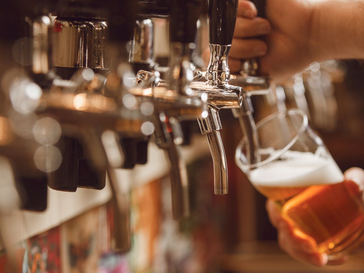 A hand pours beer from a tap into a glass at a bar, with multiple taps visible in the background.