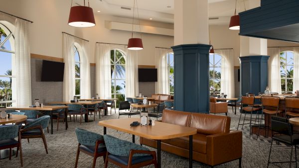 A spacious, modern dining area with tables, chairs, large windows, sofas, and hanging lights, offering a relaxed ambiance.