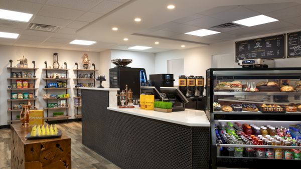 The image shows a modern coffee shop interior with a display of pastries, beverages, and snacks, alongside a counter with registers.