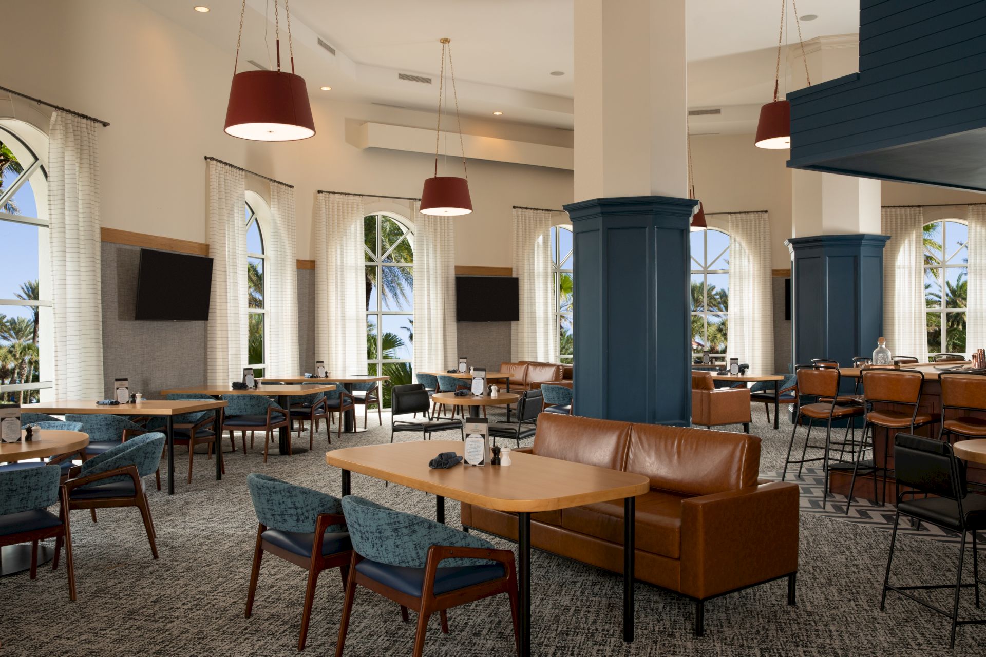 A spacious, modern restaurant with large windows, brown and blue seating, and multiple hanging lights and TVs adorn the walls.