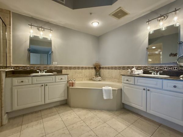 The image shows a bathroom with two sink vanities, a central bathtub, mirrors, and lights, all in a neutral color scheme.