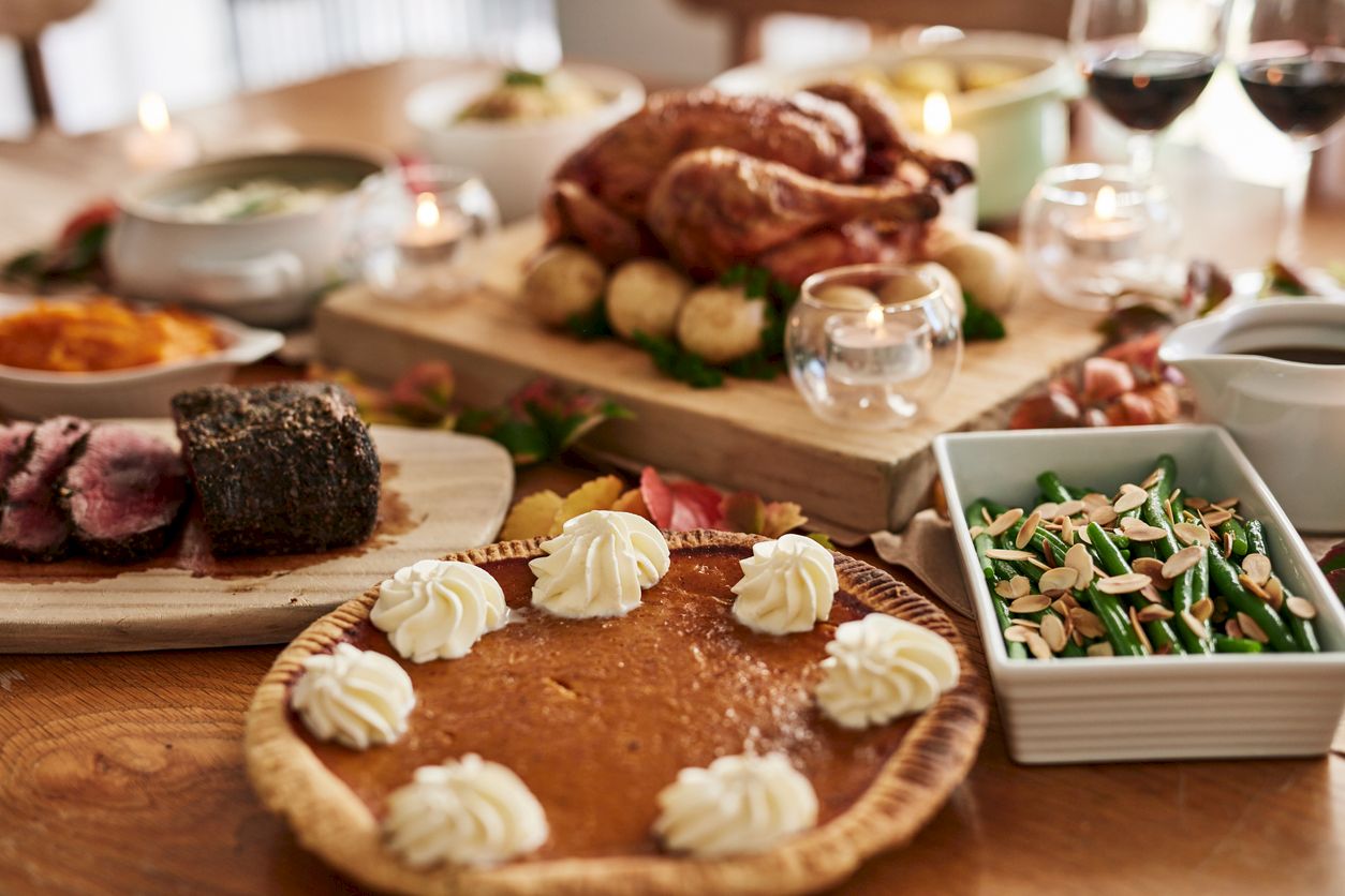 A festive dinner table spread with carved roasted meat, vegetables, and bread, plus a dessert topped with whipped cream.