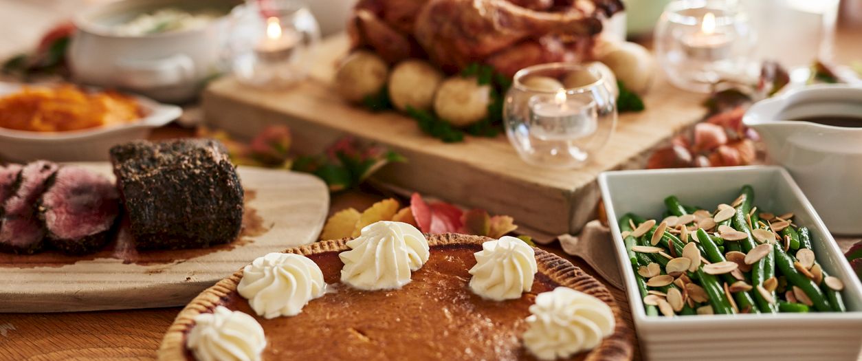 A festive dinner table spread with carved roasted meat, vegetables, and bread, plus a dessert topped with whipped cream.