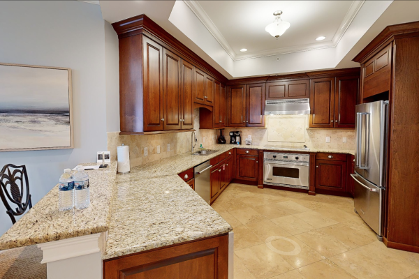 A modern kitchen with wooden cabinets, stainless steel appliances, granite countertops, and a neutral color scheme on the walls and floor.
