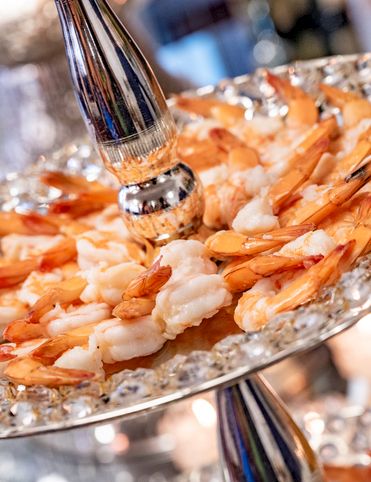A silver serving platter piled with orange shrimp and other seafood, with a shiny serving spoon in the foreground.