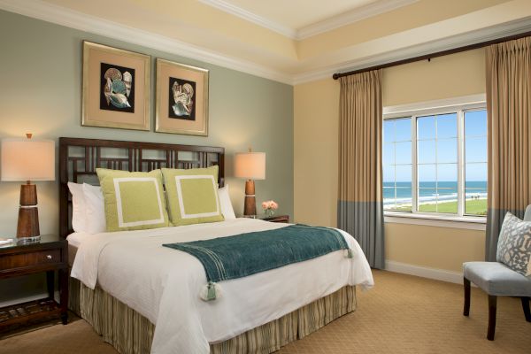 A cozy bedroom with a large bed, elegant decor, ocean-view window, and calming colors.