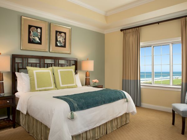 A cozy bedroom with a large bed, elegant decor, ocean-view window, and calming colors.