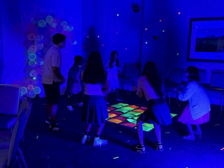 A group of people are enjoying a glow-in-the-dark dance floor with colorful lights in a dimly lit room.