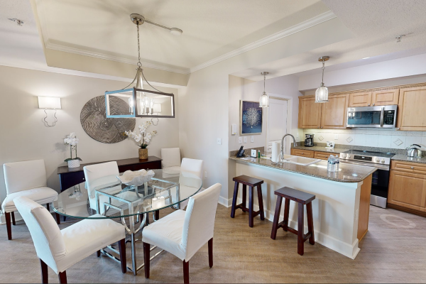 A modern kitchen dining area with wooden cabinets, granite countertops, and a glass table surrounded by white chairs.