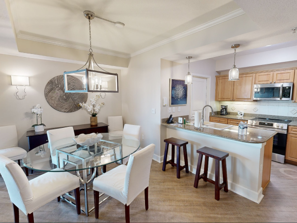 A modern kitchen dining area with wooden cabinets, granite countertops, and a glass table surrounded by white chairs.