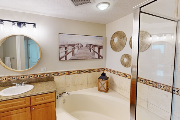 A bathroom with a round mirror, sink, tub, decorative wall art, and a framed picture of a boardwalk.