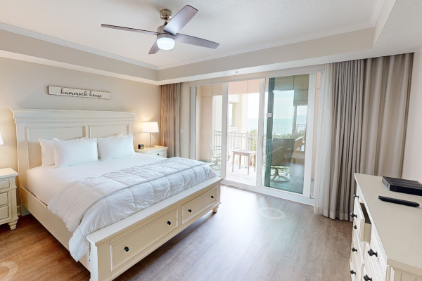 A bedroom with a double bed, lamps, fan, TV, dresser, and balcony access, featuring a sign saying "hammock house."