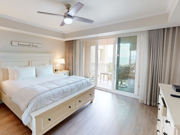 A bedroom with a double bed, lamps, fan, TV, dresser, and balcony access, featuring a sign saying "hammock house."