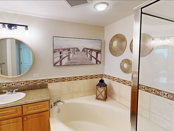 Bathroom with a bathtub, wooden vanity, round mirror, decorative art, and a framed picture on the wall.