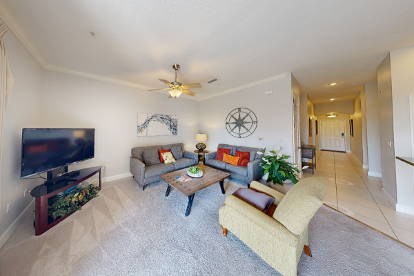 A cozy living room with sofas, a TV, coffee table, and wall decor; a hallway leads to the entrance.