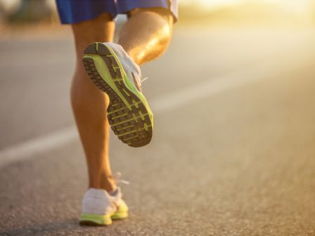 A person is running on a road with the sun setting or rising, highlighting their shoes and legs in athletic gear.