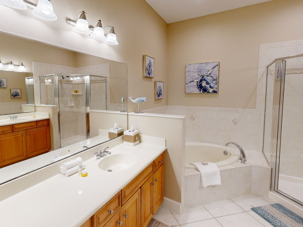 The image shows a bathroom with a large mirror, double sink, bathtub, shower, and wood cabinetry under bright lighting.