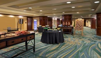 A conference or banquet area with tables set up, featuring snacks and drinks, on a carpeted floor with overhead lighting.