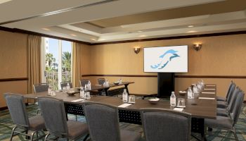 A conference room with a U-shaped table setup, chairs, notepads, water bottles, and a screen displaying a dolphin logo.
