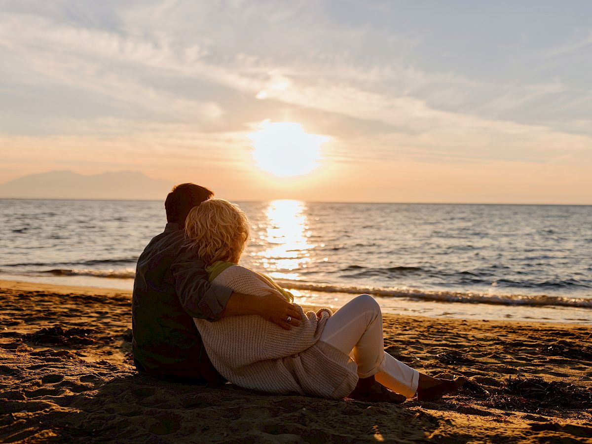 A couple is sitting on a beach, watching the sunset over the ocean.