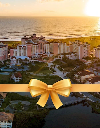 A coastal cityscape at sunset with buildings, water bodies, and a gold ribbon with a bow overlaid at the bottom of the image.